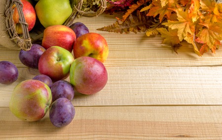 Autumn border made of apples and plums and yellow leaves on a wooden tableの写真素材