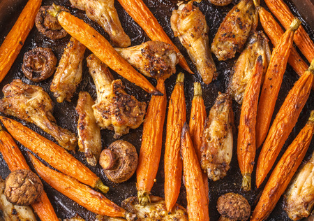 Roasted chicken wings with red carrot and mushrooms backgroundの写真素材