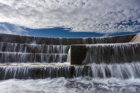 Fast running water over stairs with blue sky and white clouds on the backgroundの写真素材