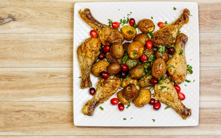 Roast chicken legs with potatoes on a white plate.の写真素材