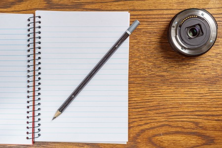 Top view of open spiral notebook with black pencil and camera lens on desk backgroundの写真素材