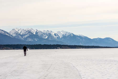 INVERMERE, CANADA - MARCH 17, 2020: ice skating men on frozen Windermere lake and rocky mountains in british columbia canadaのeditorial素材