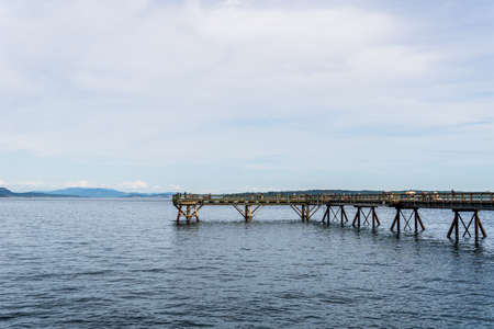 SIDNEY, CANADA - JULY 14, 2019: people on wooden pier that protrudes over the sea into the water with a cloudy skyのeditorial素材