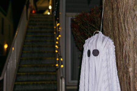 white ghost hanging on a tree during a holiday for Halloween on dark background