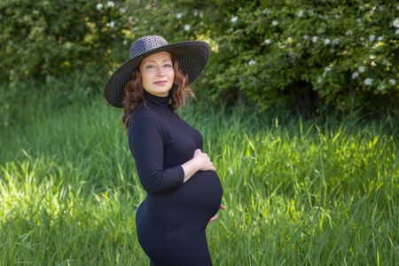 pretty pregnant woman in a black dress and hat green field park.の写真素材