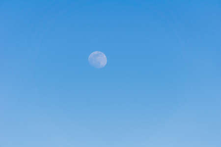 A small moon far away on blue sky in evening time as a background