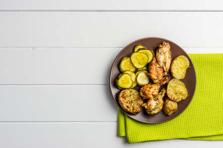 baked potatoes and chicken on a brown plate with pickled cucumbersの写真素材