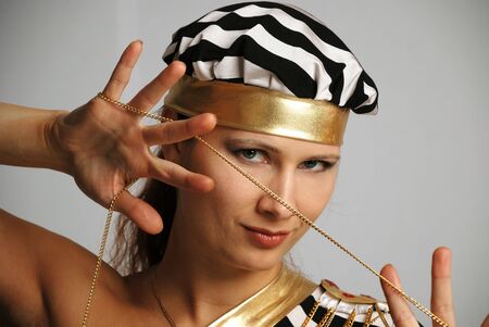 Model in stripy black-and-white cap stares and holds in spread hands goldish chain, close-up, portraitの写真素材