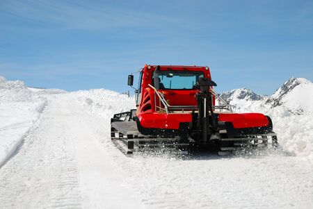 Red catterpillar tractor makes snow slope against blue sky on Pyrenees passの写真素材