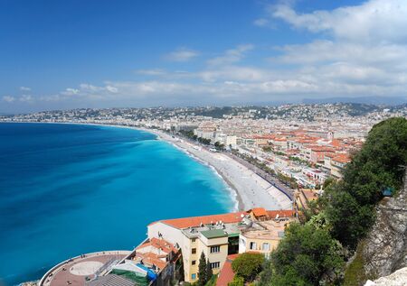 Azure sea bay and blue sky of mediterranean coast, white clouds above old and modern district of city Nice, mountains in the backgroundの写真素材