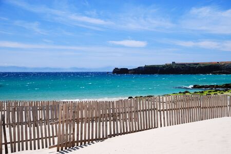 Sand beach of Tarifa with wooden sand-fences against blue sky and aquamarine seaの写真素材