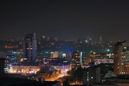 Night cityscape with orange, blue, green light spots in the middle of dark buildings, square and rectangular alight windows, high angle viewの写真素材