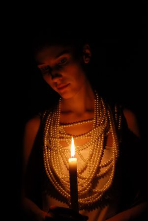 Girl with burning candle and pearl necklace in the darkの写真素材