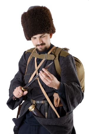 Young man is wearing vintage uniform of Russian foot Cossack in time First World War. Russian Cossak is looking over a dagger. He is dressed in woolen greatcoat, fur cap and boots. He is carried military equipment. の写真素材