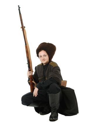 Young woman is wearing vintage uniform of Russian foot Cossack in time First World War. Russian Cossak is squatting and smiling. She is lifting a rifle. She is dressed in woolen greatcoat, fur cap and boots. の写真素材