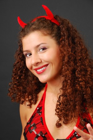 Sexy woman is smiling broadly and looking at the camera. Small red horns are in her curly hair