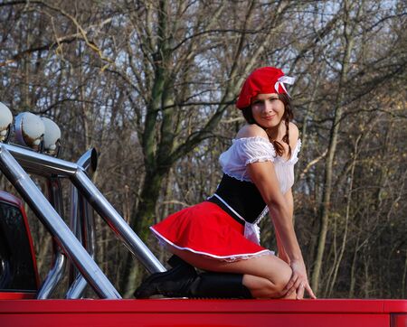 Pretty woman is sitting on the red body of big auto. She is wearing in sexy costume of Little Red...