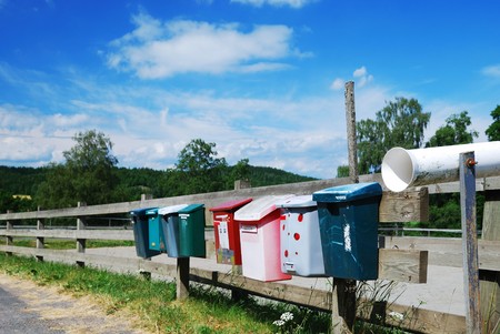 Various postboxes are hanging on the wood fence near the country road.の写真素材