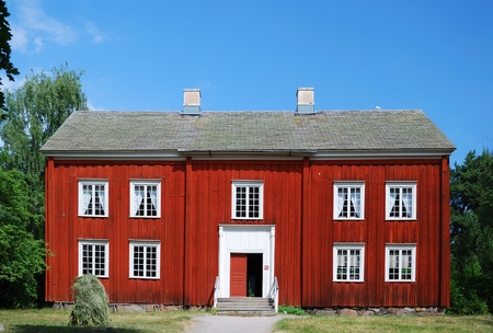 Two-storied wooden house is situated in the Scansen. In the background there are summer forest and the blue sky. The estate is built in the nineteenth century.の写真素材