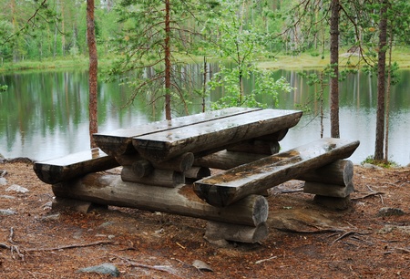 Wet wooden table and benches are made of logs. The resting place is near river in taiga forest. 