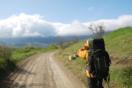 Hiker is shooting a landscape by video camera. He is standing on the natural road. He is carrying a large rucksack.の写真素材