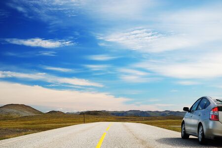 Asphalt road with yellow line is running along the mossy hills. Modern car is parked aside from the...