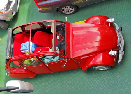 Vintage car is parked on the green floor of ferry. The small automobile is photographed from above....