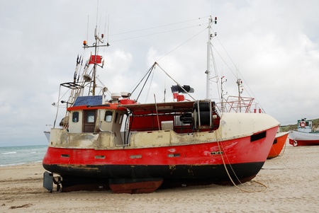 Fishing ship is still on the sand of Danish seacoast. The sky is overcast.