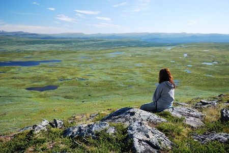 A woman is sitting on the top of the hill in Swedish Lapland. There are a lot of small lakes on the...