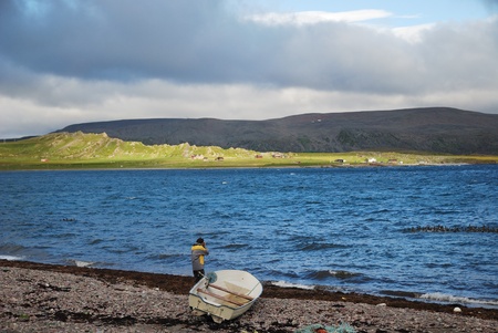 There are a man with a boat on the northernmost shore of Europe. The dark blue sea is reflecting the...