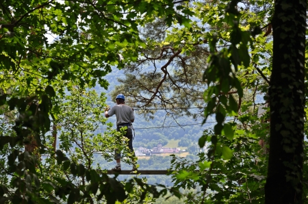 Teenage boy is climbing on the trapeze bar at the rope parkour outdoors  
