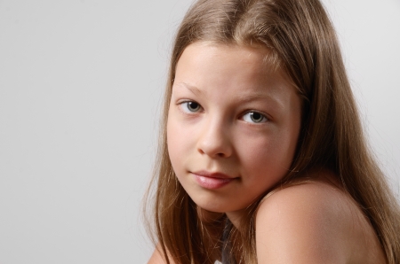 A teenage girl is photographed close-up on the gray background. The sad teen is looking at the camera. Her fair long hair are flowing. There is a copy space.の写真素材