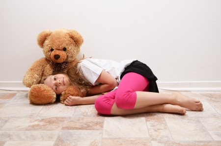 A blonde girl is lying on the floor. She is putting her head on the big teddy bear and looking at the camera.の写真素材