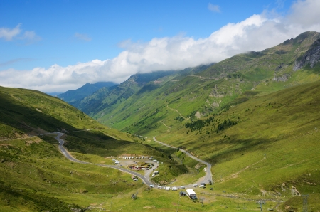 There are green slopes of mountains from the pass of Tourmalet in Pyrenees. Remote peaks are covered with white clouds. A serpentine road is prepared for the cycle race.の写真素材