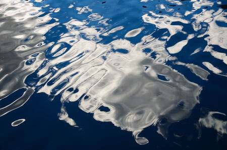 White clouds and the blue sky are reflected with waving surface of the blue water の写真素材