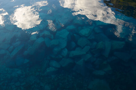 White clouds and large stones are in the blue transparent water of the mountainous lake の写真素材
