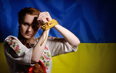 The young woman is rising her bound arms against the national Ukrainian flag. She is wearing a shirt embroidered.の写真素材