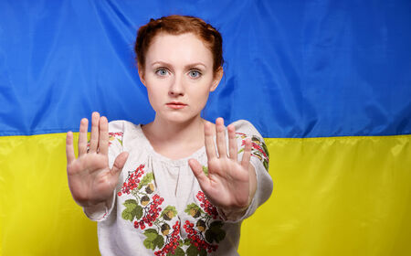 The frightened young woman is making a gesture of defence against the national Ukrainian flag. She is wearing a shirt embroidered.の写真素材