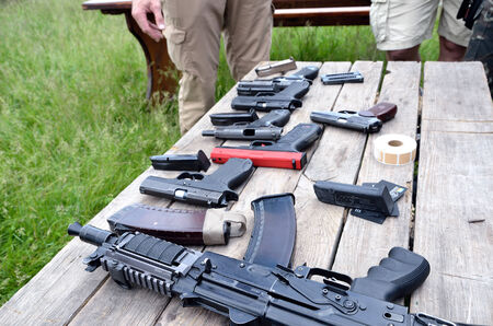 A submachine gun, pistols and other firearm are laid out on the table outdoors.のeditorial素材