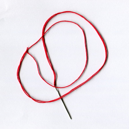 A tapestry needle with red cotton spun strand are on white background.