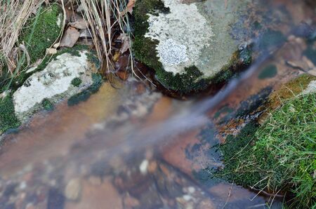 A clear brook is running over mossy pebbles in the mountain slope. It is photographed closeup at long shutter speed.の写真素材
