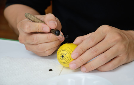 The human hands are writing with melting wax the traditional ornament on the  dyed egg. The Easter...