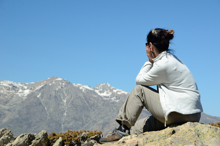 A female tourist is sitting on the top. She is looking at the highest Corsican mountain Monte Cinto.の写真素材