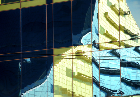The colored mirror surface reflects a black shadow and the modern building of the Latvian national...
