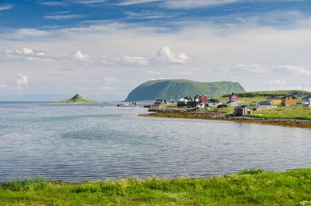 Grassy shore of the bay with a small village in the island Mageroya in the north island Mageroya