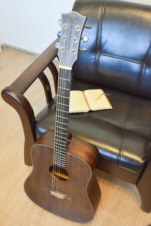 Acoustic six-string guitar, vintage leather armchair and vintage notepad in the interiorの写真素材