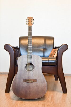 Acoustic six-string guitar, vintage leather armchair and vintage notepad in the interiorの写真素材