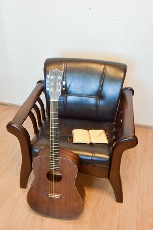 Acoustic six-string guitar, vintage leather armchair and vintage notepad in the interiorの写真素材