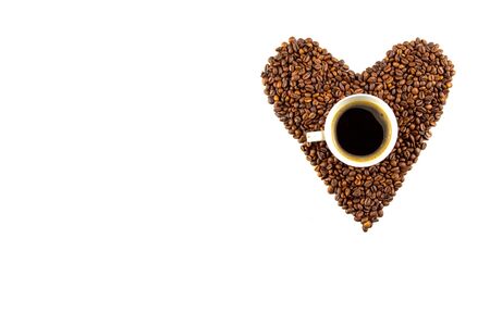 Cup of coffee and a heart shape made of roasted coffee beans isolated on white backgroundの写真素材
