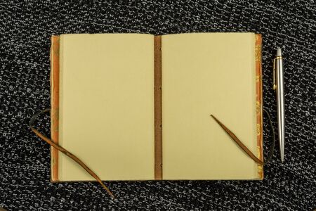 open vintage notebook and pen on a background of knitted fabric in black top view flat layの写真素材